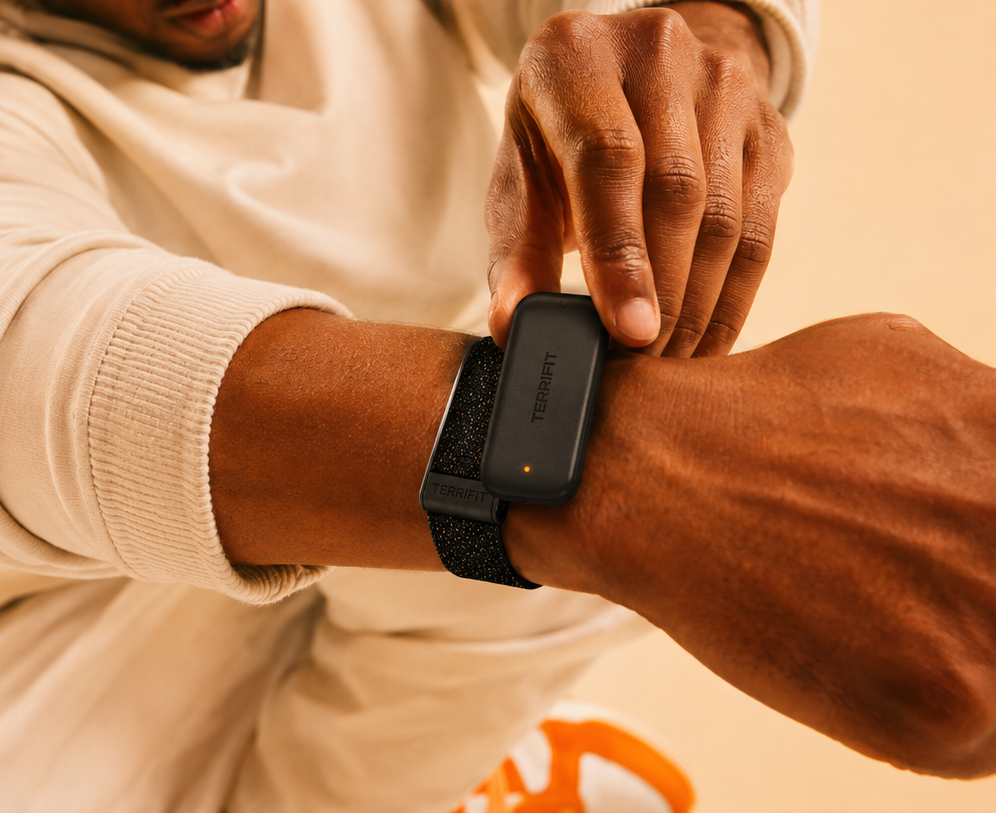 Terrifit V1 PowerPack sliding onto the band on someone's wrist, a small matte black module with a single amber charge light
