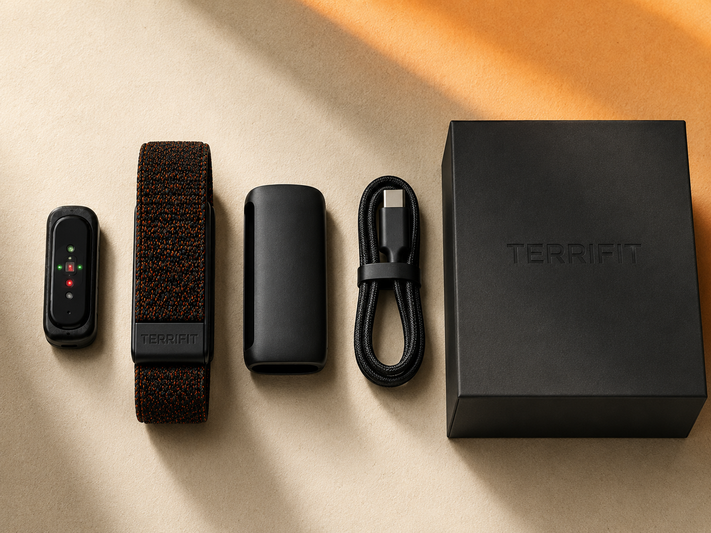 Flat lay of everything in the Terrifit V1 box on warm paper: sensor module, woven strap, PowerPack and braided USB-C cable, arranged on a grid
